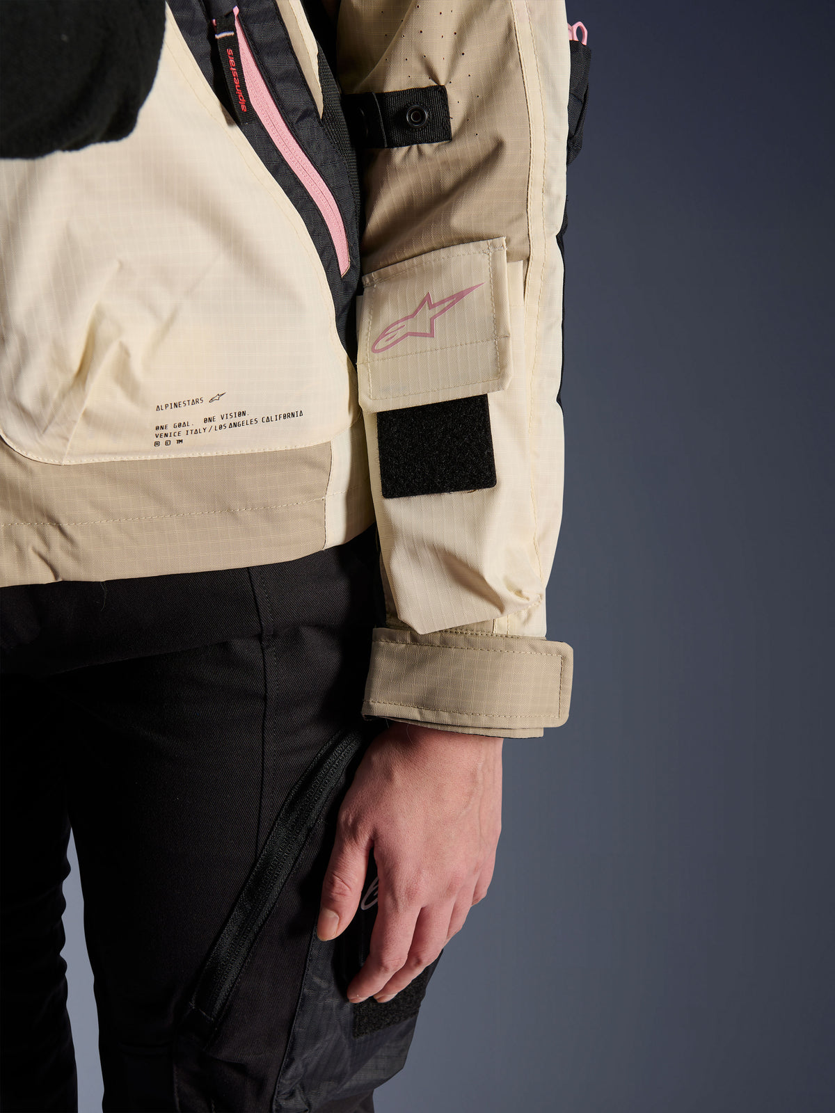 Alpinestars Molly Air Jacka, urban motorcykeljacka för dam, Sand Pink Almond, närbild från sidan som visar ärmficka med rosa logotyp, svart kardborrepatch och varumärkets missionstext på nedre ryggen, lätt ripstop-material