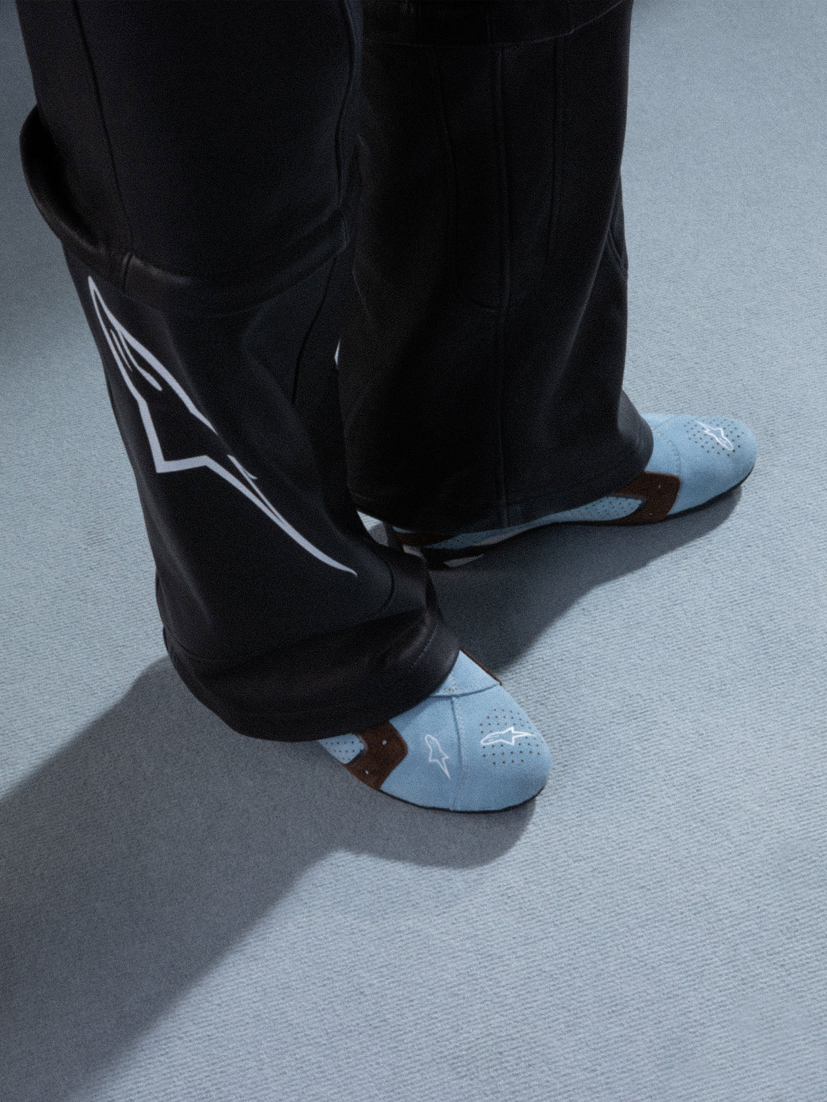 Alpinestars RSRV Starline skor, ljusblå perforerade sneakers med bruna detaljer, premium läderkonstruktion med vit logotyp, visade med svarta läderbyxor med vita designelement