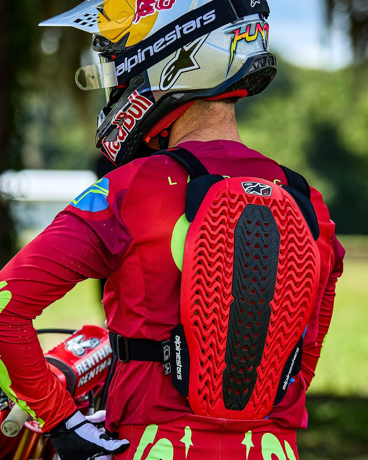 Alpinestars A-5 Plasma bröstskydd, motocrossförare sedd bakifrån med ett rött och svart ryggskydd med ventilerad bikakestruktur, buren över en röd långärmad tröja och en Red Bull-märkt hjälm.