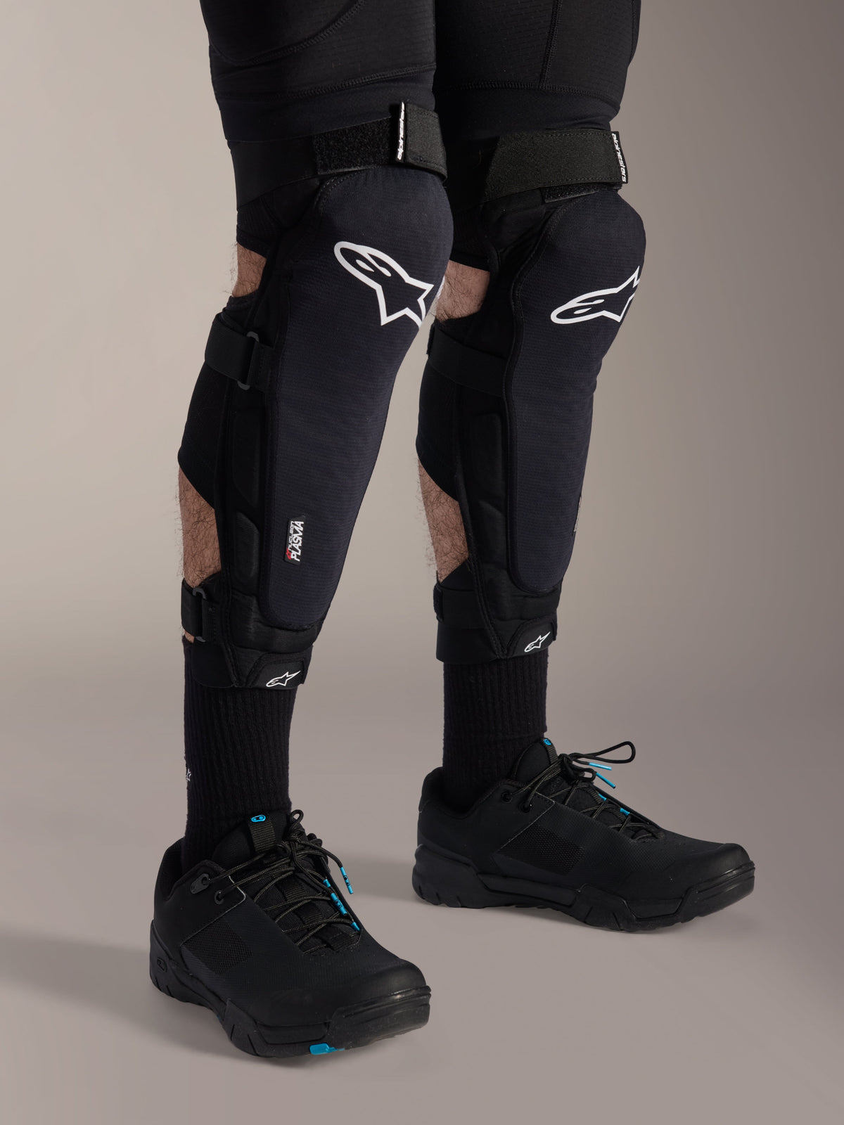 Alpinestars A-Impact Plasma Pro knäskydd, svarta och vita, med Nucleon PLASMA-teknologi, bärs med svarta strumpor och svarta mountainbikeskor, säkra kardborreband, ergonomisk skyddsutrustning för terrängcykling