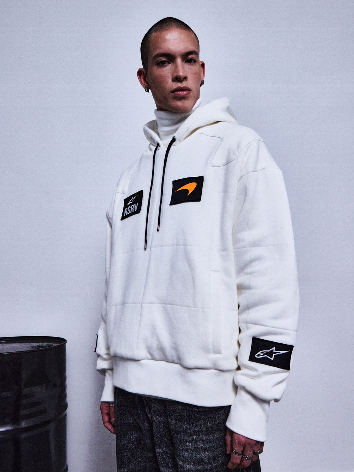 Alpinestars RSRV Rival Hoodie, vit premium streetwear-hoodie med svarta patches, orange swoosh-detalj och RSRV-logotyp, unisex lyxkollektion, person iklädd hoodie med polotröja