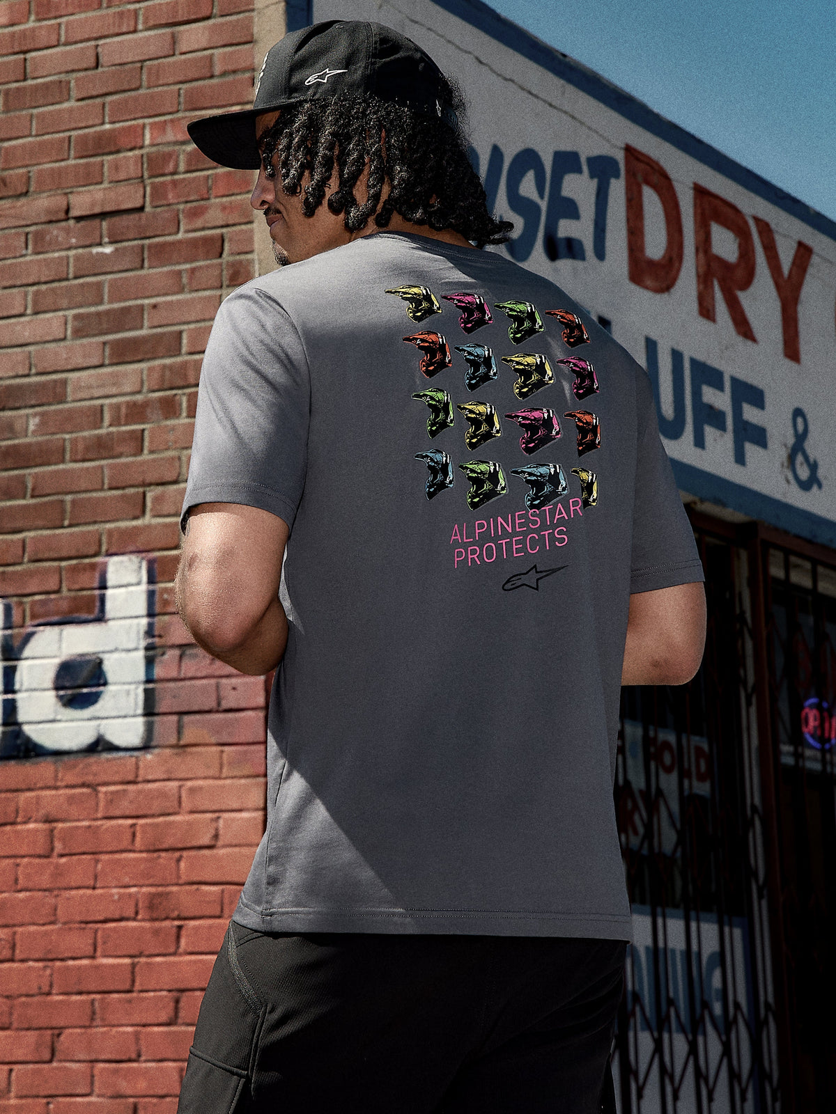 Alpinestars Pop Helmet CSF Tee, kortärmad t-shirt, koksgrå, rygggrafik med färgglada M10-hjälmar och rosa 'ALPINESTAR PROTECTS'-text, avslappnad motorsport-inspirerad streetwear