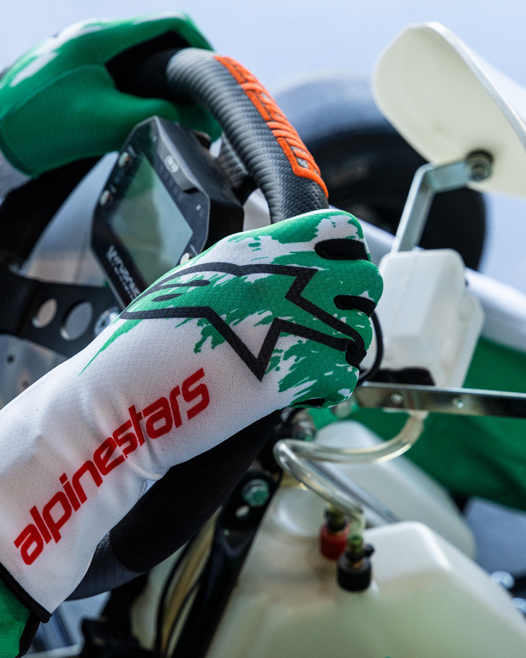 Alpinestars Tech-1 K V3-handskar i vitt, grönt och rött, förarens händer som greppar en kartingratt, grön sublimerad stänkdesign, svart stjärnlogotyp och röd Alpinestars-text på manschetten, professionell kartingutrustning