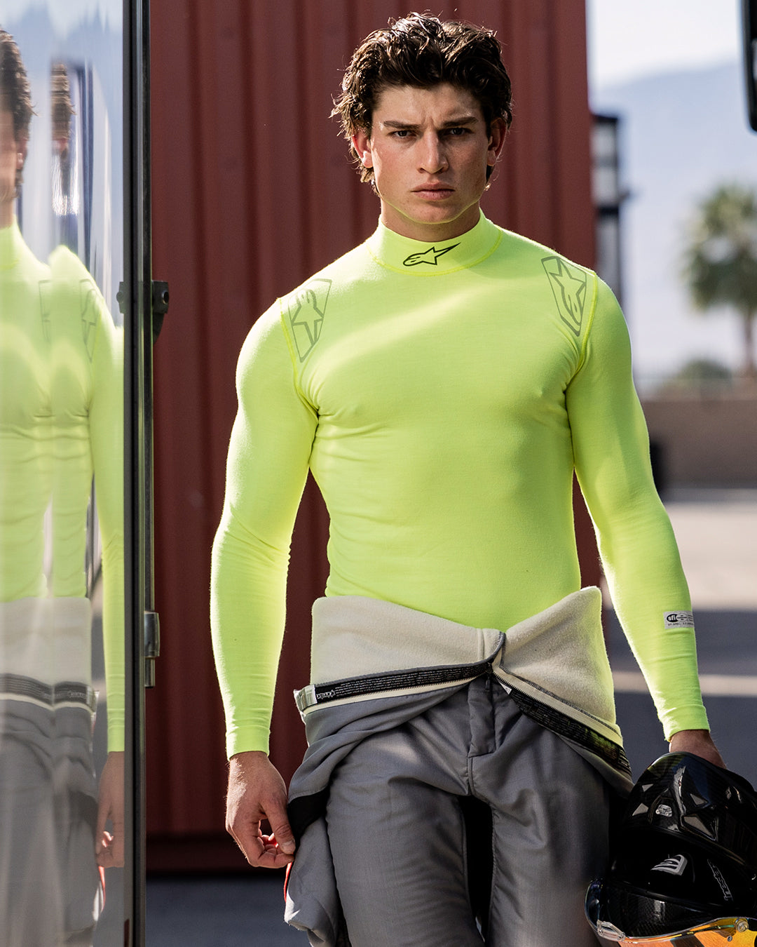 Alpinestars ZX Evo V3 Top - Långärmad, tekniskt underställ för bilracing, Yellow Fluo, bärs av en manlig förare med en grå racingoverall knuten runt midjan, håller en svart hjälm, med Alpinestars-logotyp på halsen och axlarna, teknisk fuktavledande utrustning för motorsport