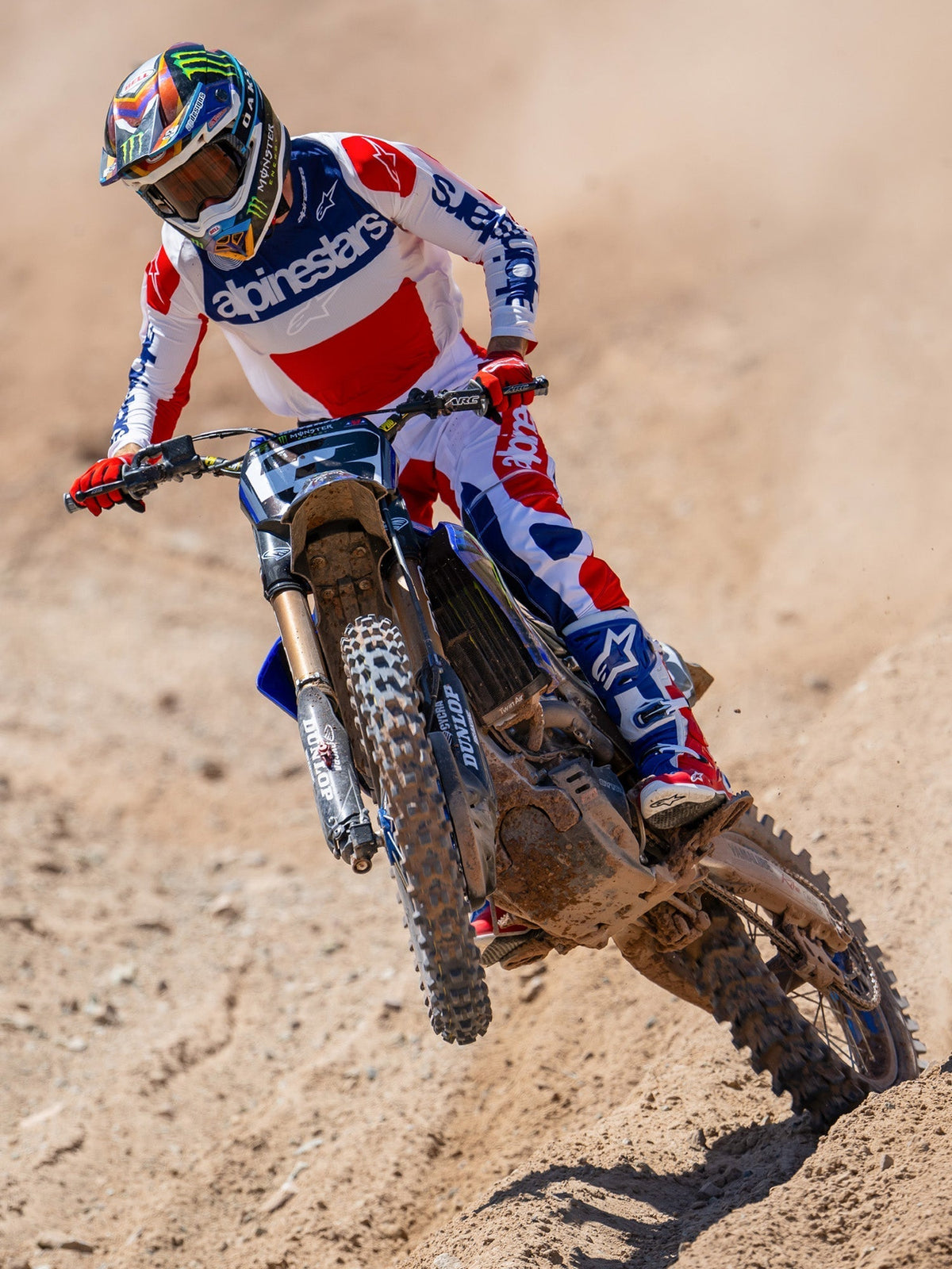 Alpinestars Limited Edition Techstar Fortitude byxor, motocrossbyxor, klarröd, vit och blå, bärs av en förare i action på en grusbana, med matchande tröja och stövlar, prestationsinriktad racingutrustning för terrängkörning