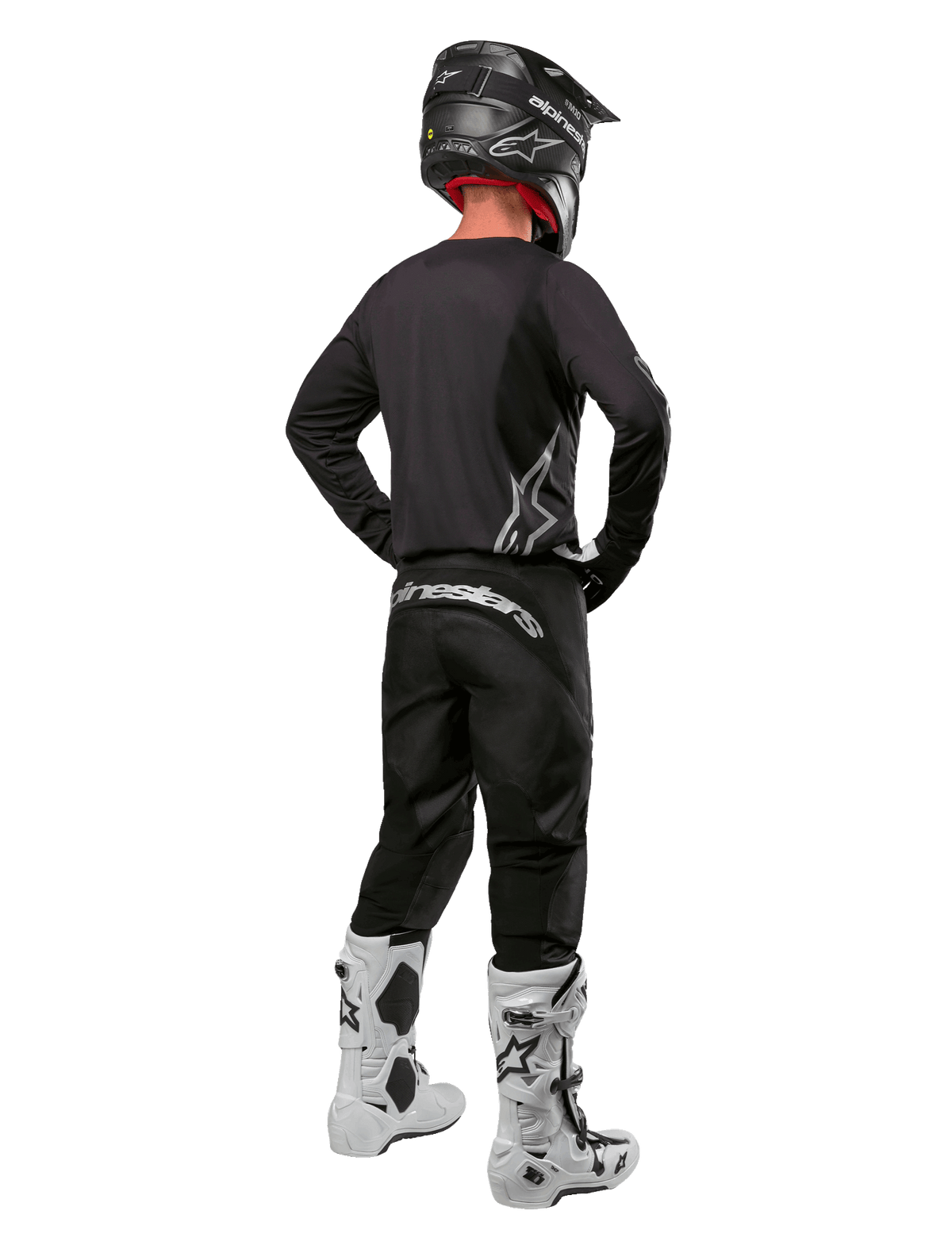 Alpinestars 2024 Fluid Graphite utrustningsset, motocrossförare sedd bakifrån, grafitgrå tröja och byxor med silverfärgade Alpinestars-logotyper, svart hjälm och vita motocross-stövlar, utrustning med atletisk passform för terrängkörning