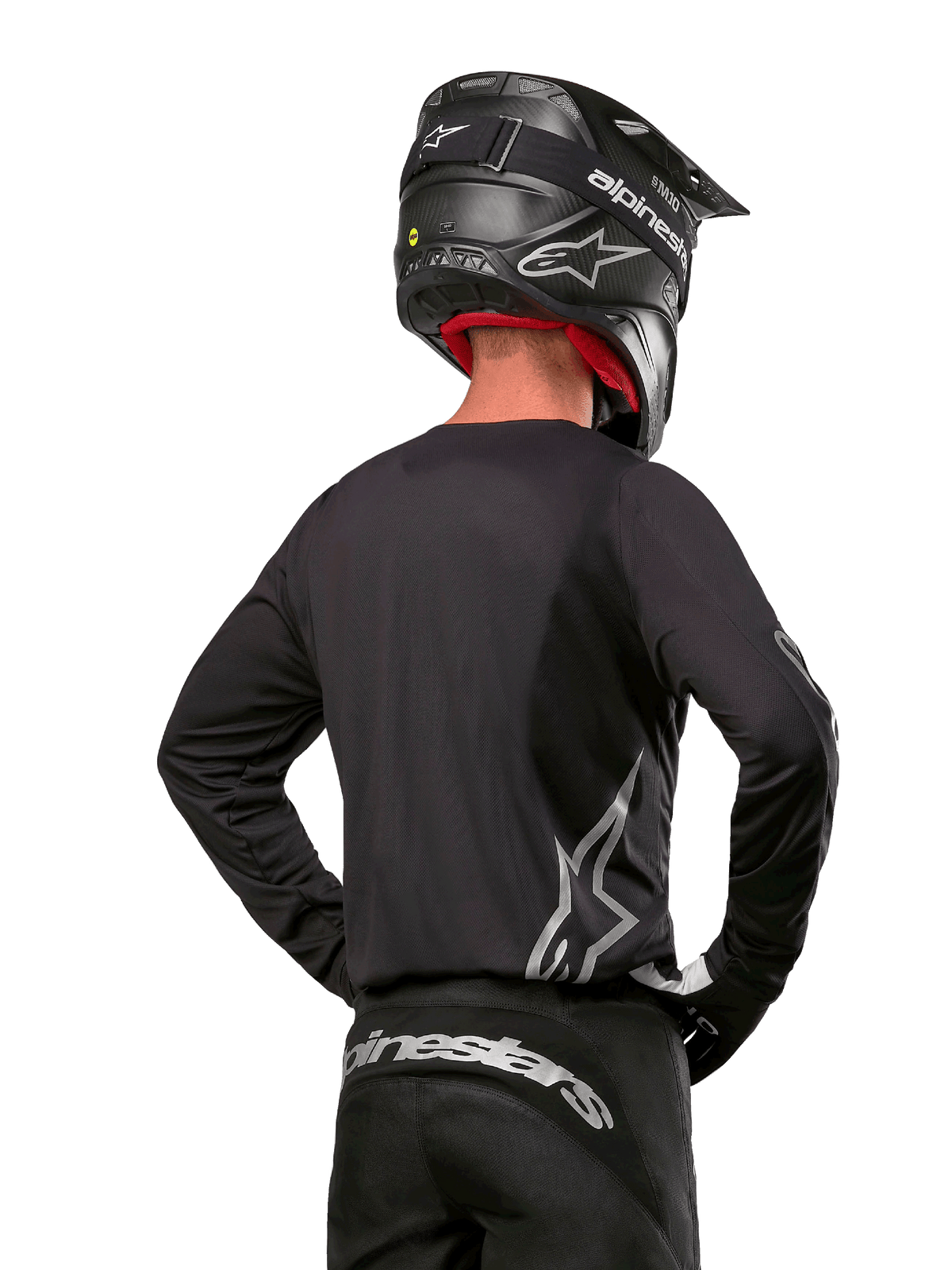 Motocrossförare sedd bakifrån i Alpinestars 2024 Fluid Graphite Jersey i Black Silver, med en stor silverlogotyp på sidan, kombinerad med en svart hjälm i kolfiberstruktur och svarta byxor, professionell racingutrustning för terrängkörning