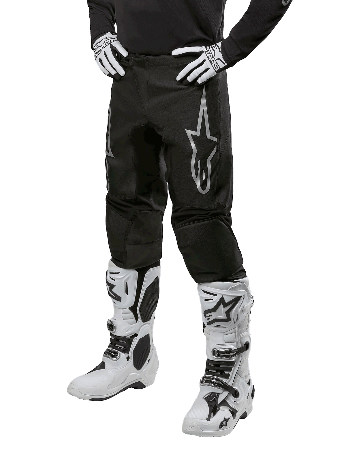 Alpinestars 2024 Fluid Graphite byxor, motocrossbyxor, grå och svarta, bärs med vita och svarta motocross-stövlar och handskar, med en stor silverfärgad Alpinestars-logotyp på låret, atletisk sportpassform för terrängkörning