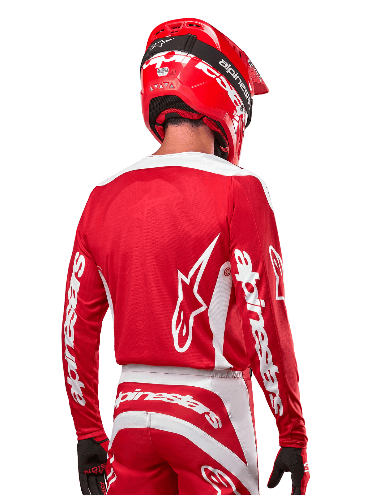 Motocrossförare iklädd Alpinestars 2024 Fluid Lurv Jersey, Mars Red och vit, vy bakifrån som visar vit Alpinestars-logotyp på ryggen och branding på ärmarna, matchad med röd hjälm och svarta handskar, professionell utrustning för terrängkörning