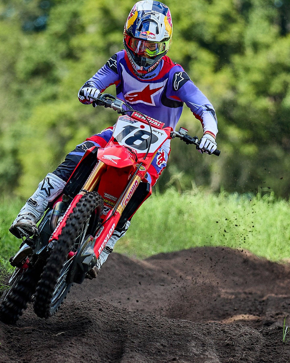 Motocross rider on a red Honda dirt bike, wearing Alpinestars 2025 Fluid Wurx Jersey in Purple and Bright Red, matching pants, white boots, and Red Bull helmet, navigating a dirt track turn.
