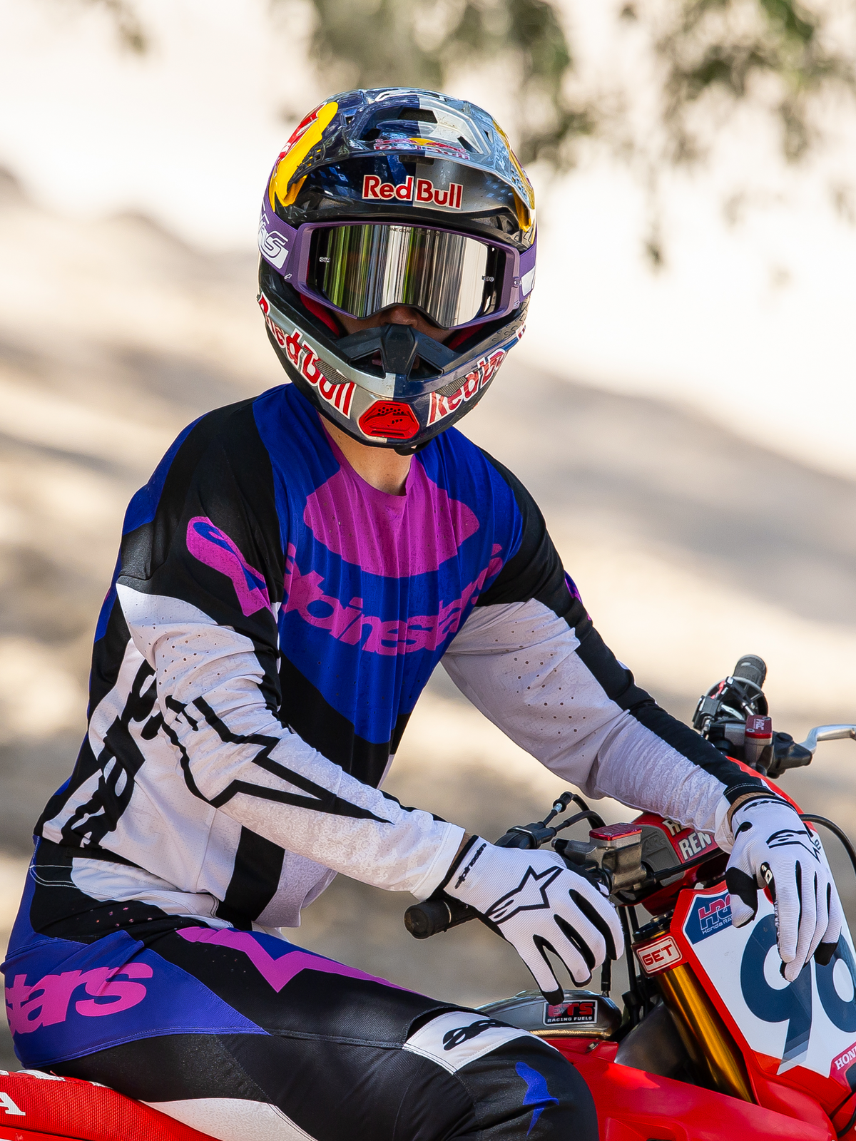Motocrossförare på en röd motocrosscykel, Limited Edition HUNTA96 XXV Supertech Vision-glasögon i lila och vitt med silverspegel-linser, matchande lila, svart och vit Alpinestars-tröja och byxor, Red Bull-hjälm, vita handskar, koordinerad professionell motocrossutrustning