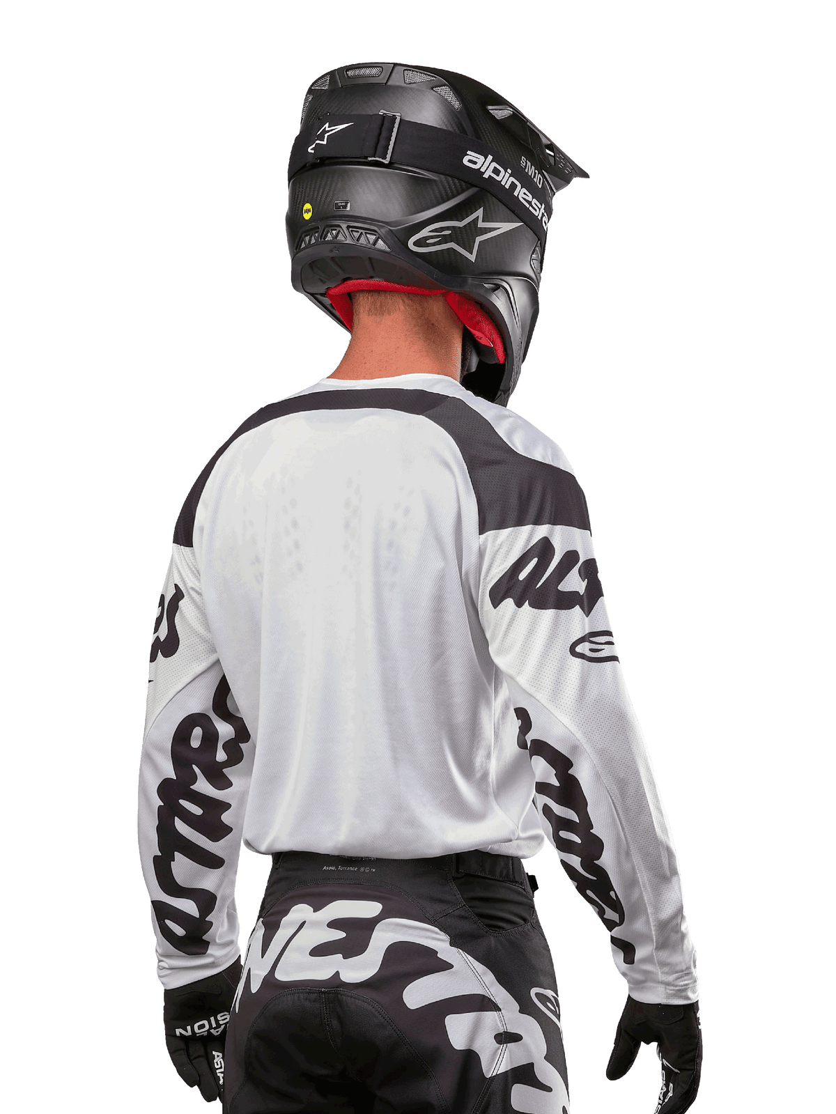 Alpinestars 2024 Racer Hana-tröja, vit och svart, vy bakifrån som visar ergonomisk passform och framträdande logotyper på ärmarna, kombinerad med en svart motocrosshjälm och matchande svartvita byxor, högpresterande racingutrustning för terrängkörning
