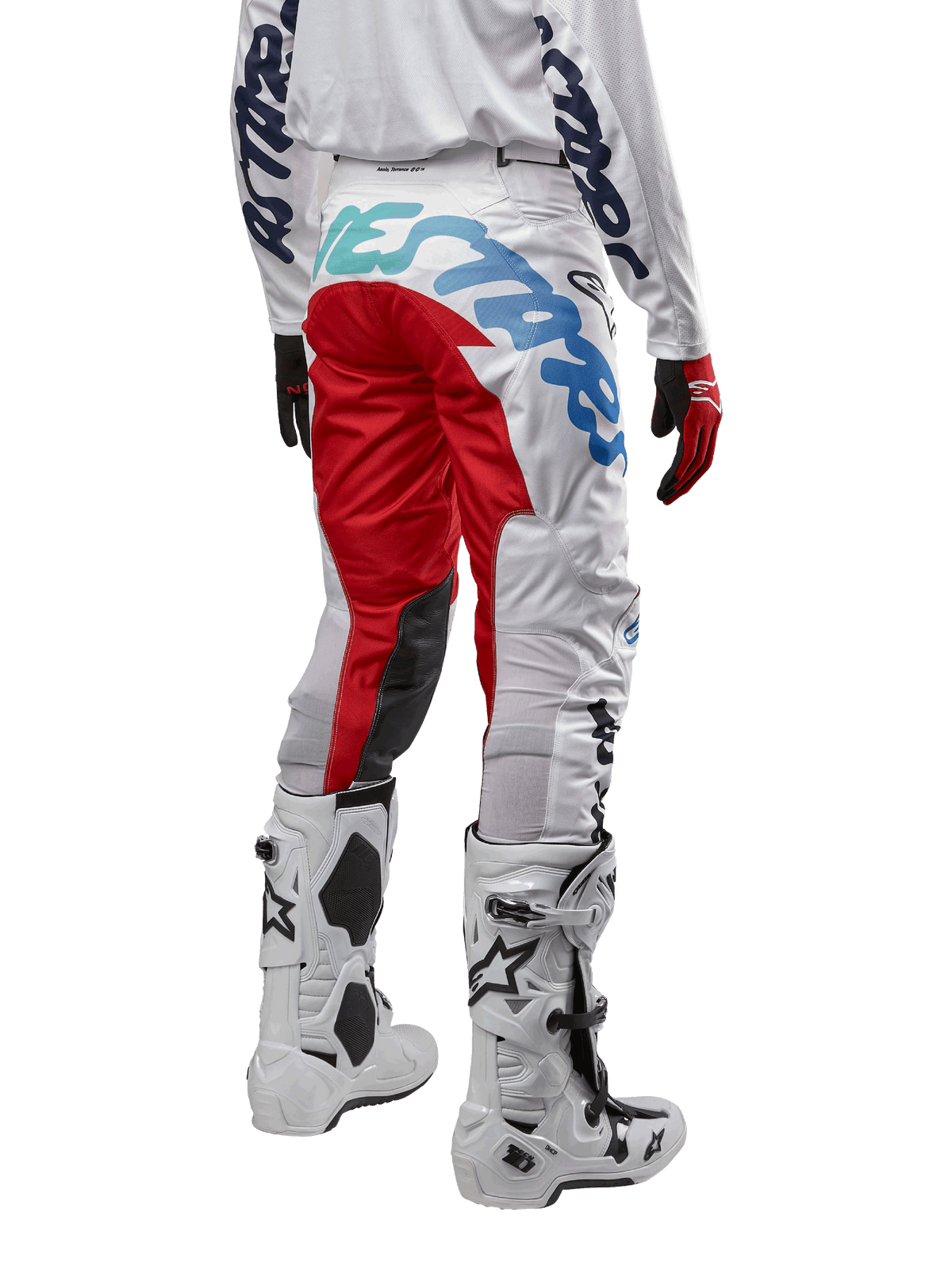 Alpinestars 2024 Racer Hana byxor, motocrossbyxor, vita flerfärgade med röda och blå detaljer, vy bakifrån som visar stor logotyp på baken, bärs med vita och svarta motocross-stövlar, designade för offroad-prestanda och hållbarhet