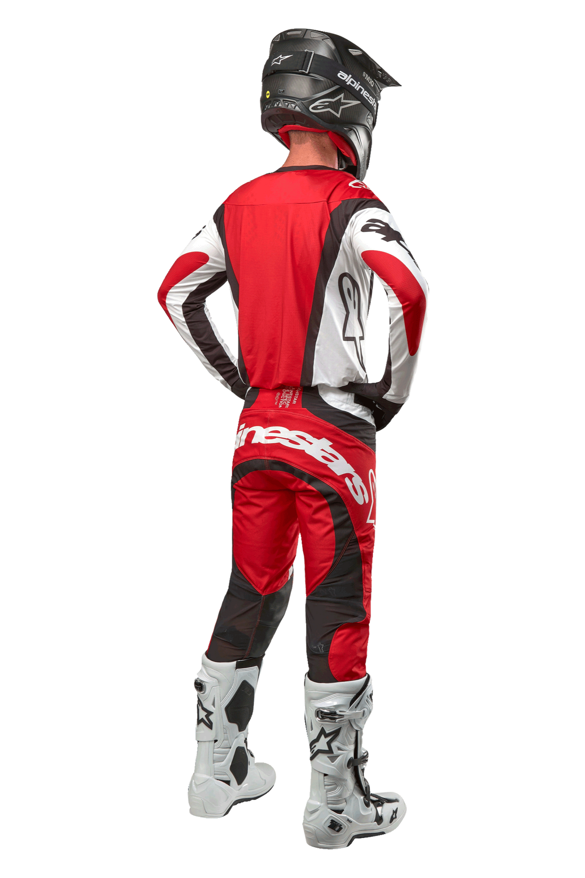 Alpinestars 2024 Techstar Ocuri byxor, motocrossbyxor, Mars Red White Black, vy bakifrån av en motocrossförare klädd i full tävlingsutrustning, inklusive matchande tröja, svart hjälm och vita och svarta stövlar, som framhäver Alpinestars logotyper och den hållbara materialkonstruktionen.