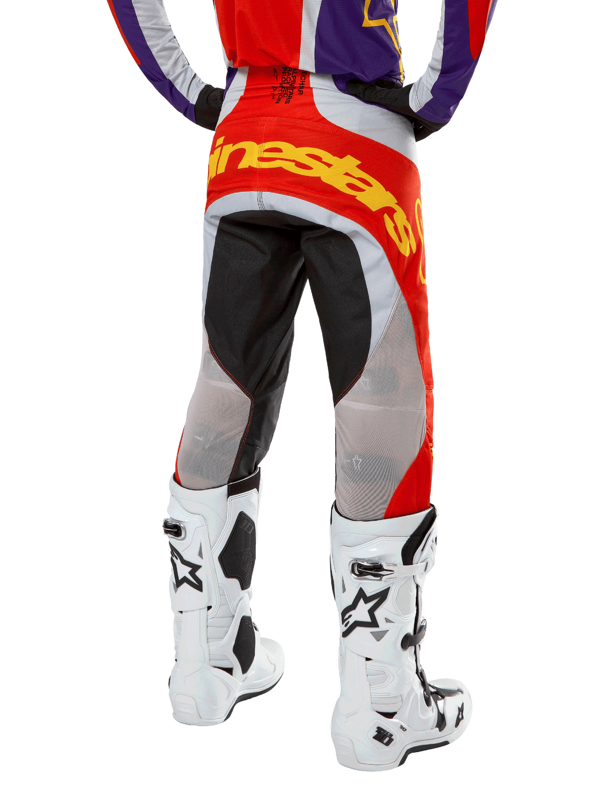 Alpinestars 2024 Techstar Ocuri byxor, motocrossbyxor, Hot Orange, lila och svarta, bakifrån från midjan och ner, stor gul logotyp över sätet, svarta och grå tekniska paneler, matchade med vita motocross-stövlar.