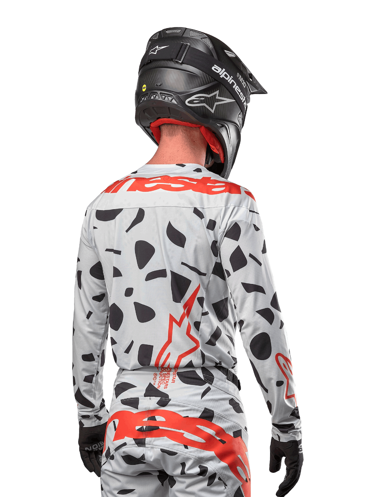 Motocrossförare sedd bakifrån i Alpinestars 2024 Techstar Rantera-tröja i Haze Gray Camo, med en ljusgrå bas med svarta grafiska fläckar och framträdande röda Alpinestars-logotyper på ryggen och axlarna, matchad med matchande byxor och en svart hjälm.