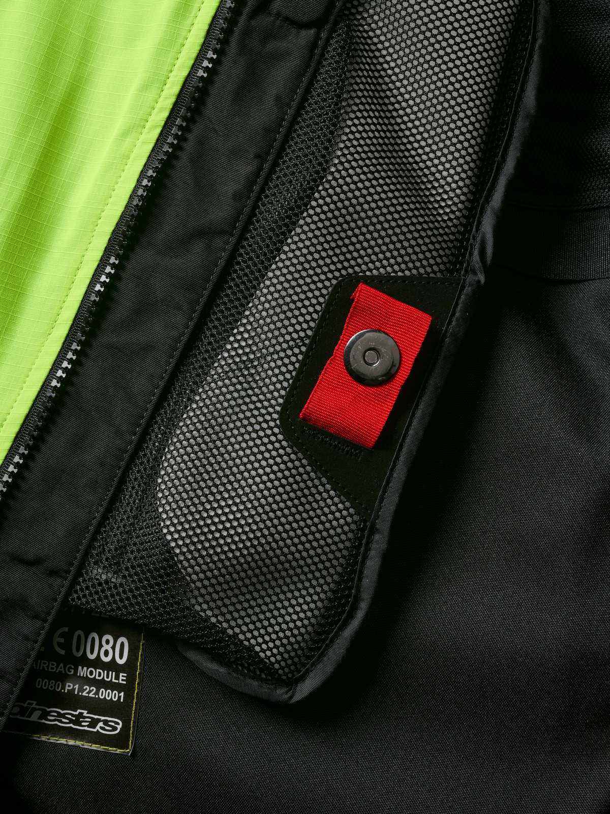 Alpinestars Tech-Air® 3 V2 System detalj, närbild av invändig nätficka med röd dragflik och tryckknapp, färgstark gul fluo-panel, svart textilkonstruktion som visar airbag-modulens etikett och dragkedja