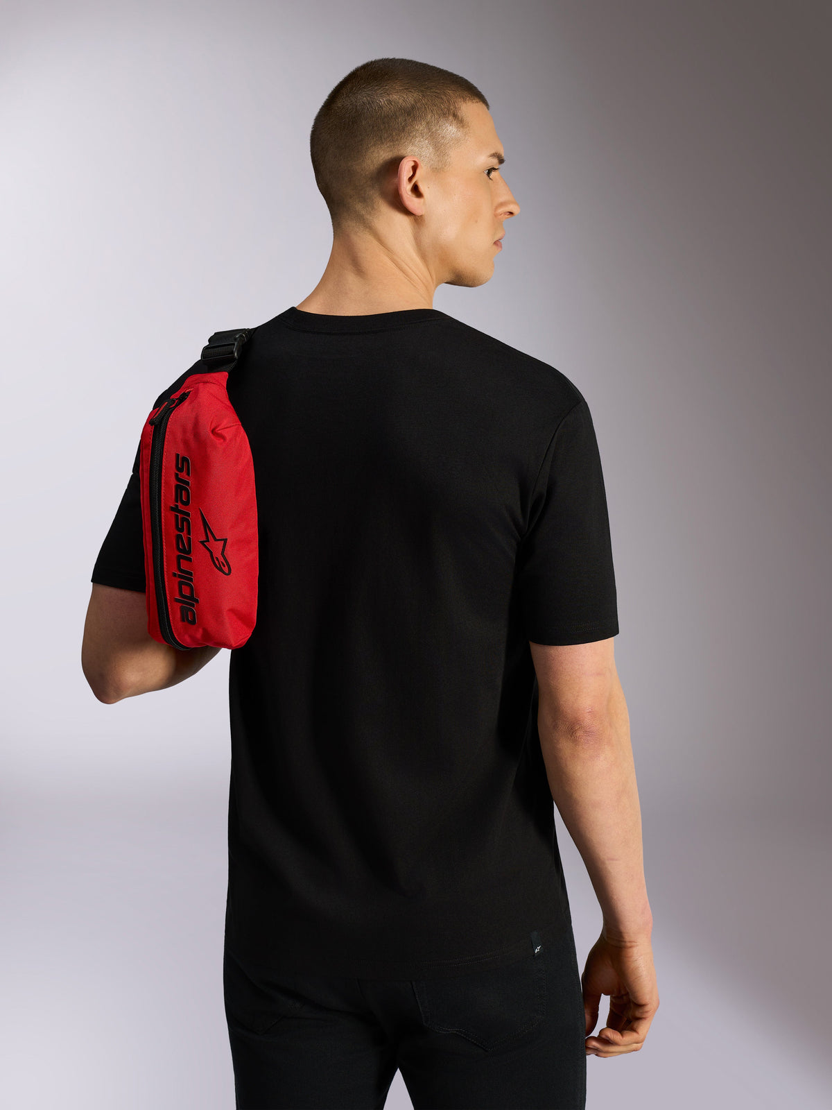Alpinestars Only Linear höftväska, röd och svart, bärs över axeln som en slingväska av en modell i en svart t-shirt, med vertikal dragkedja och svart Alpinestars-logotyp, hållbar urban accessoar.