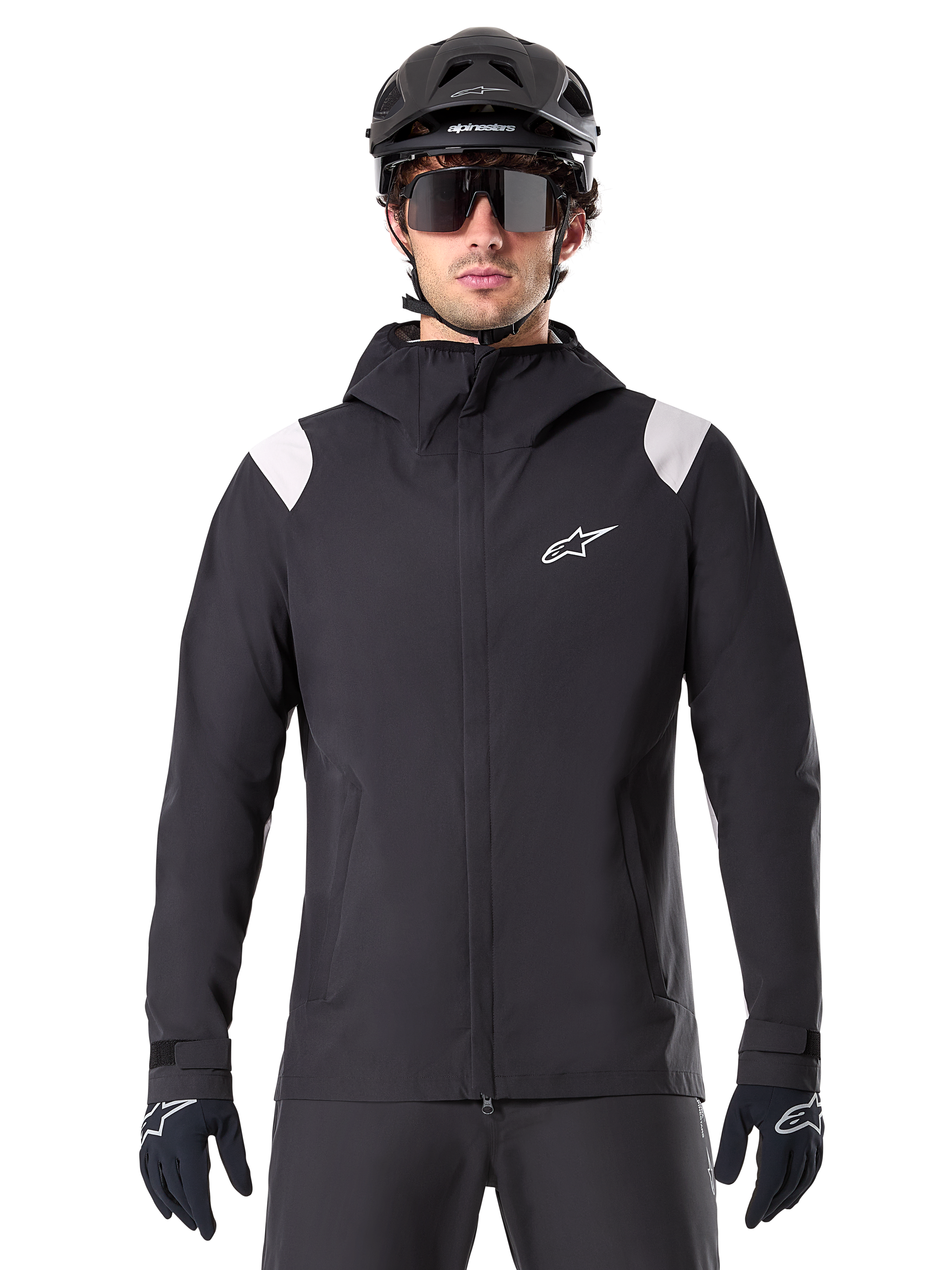 Alpinestars A-Dura regnjacka, MTB-regnjacka, svart med vita axelpaneler, bärs med svart MTB-hjälm, solglasögon och handskar, vattentät design med huva och dragkedja fram, sportig friluftsutrustning för cykling