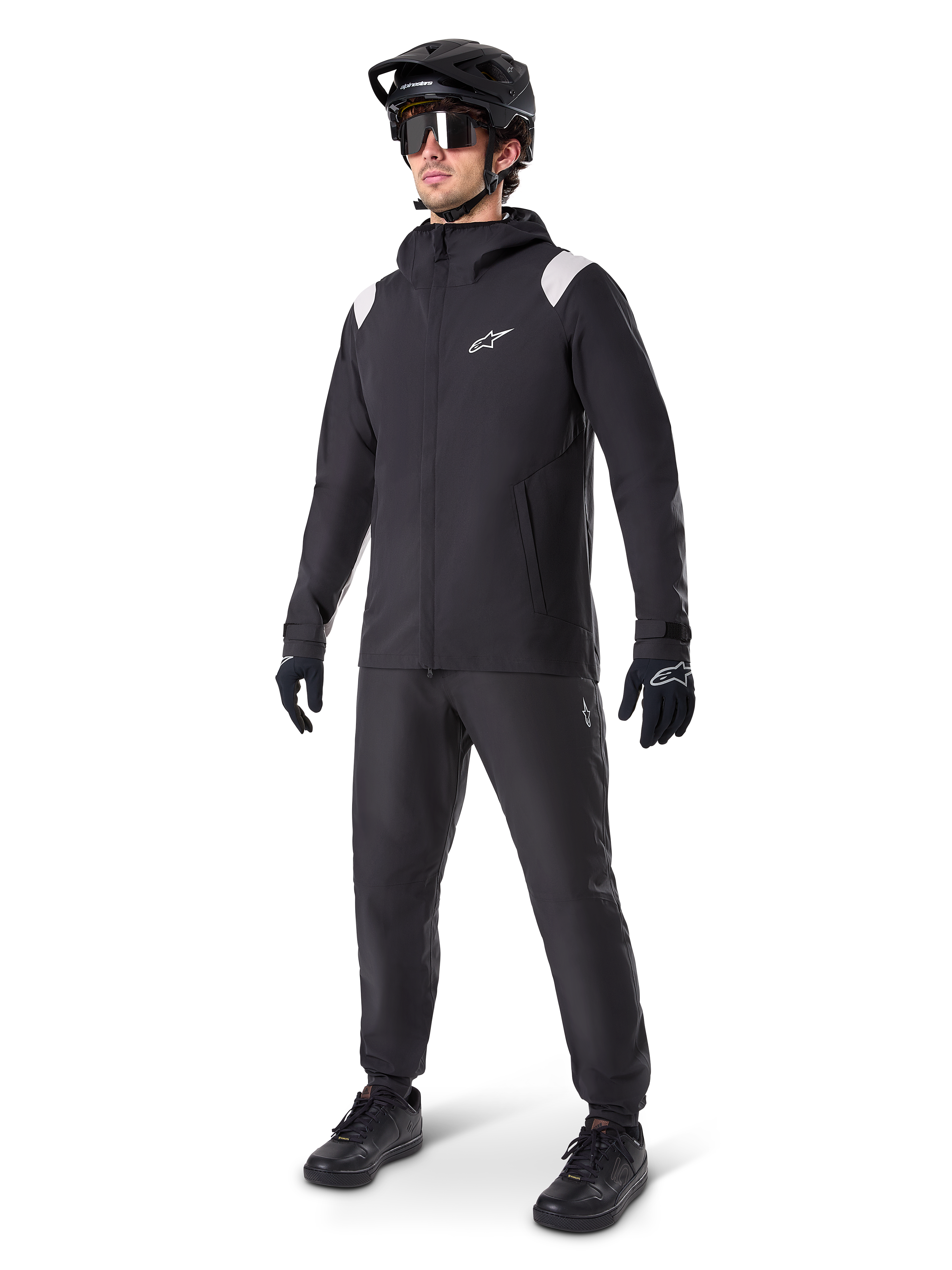 Alpinestars A-Dura regnjacka, svart regnjacka för mountainbike, med vita axeldetaljer, bärs av en cyklist med matchande svart MTB-hjälm, solglasögon, handskar och byxor, teknisk cykeloutfit för alla väder