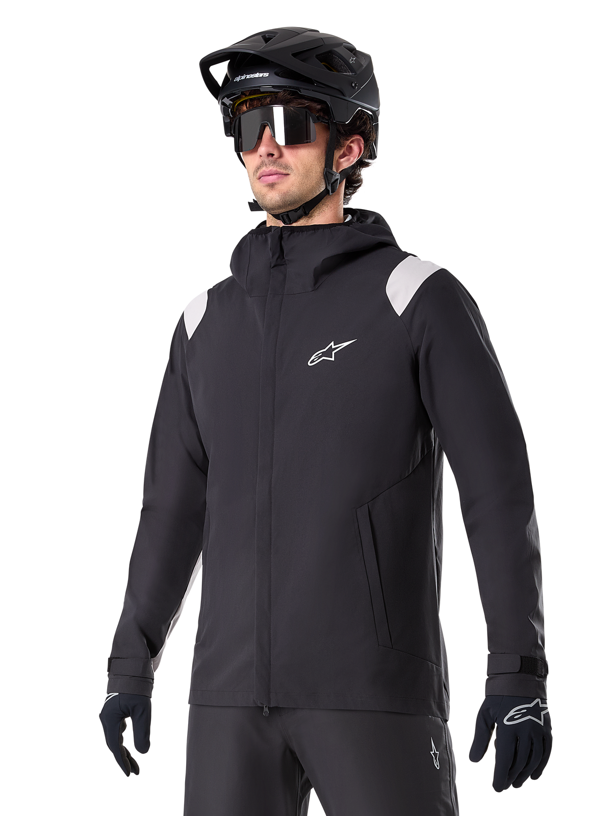 Alpinestars A-Dura regnjacka, regnjacka för mountainbike, svart med ljusgrå axeldetaljer, bärs av en cyklist med svart MTB-hjälm och solglasögon, vit logotyp på bröstet, vattentät konstruktion, matchad med svarta byxor och handskar för terrängcykling