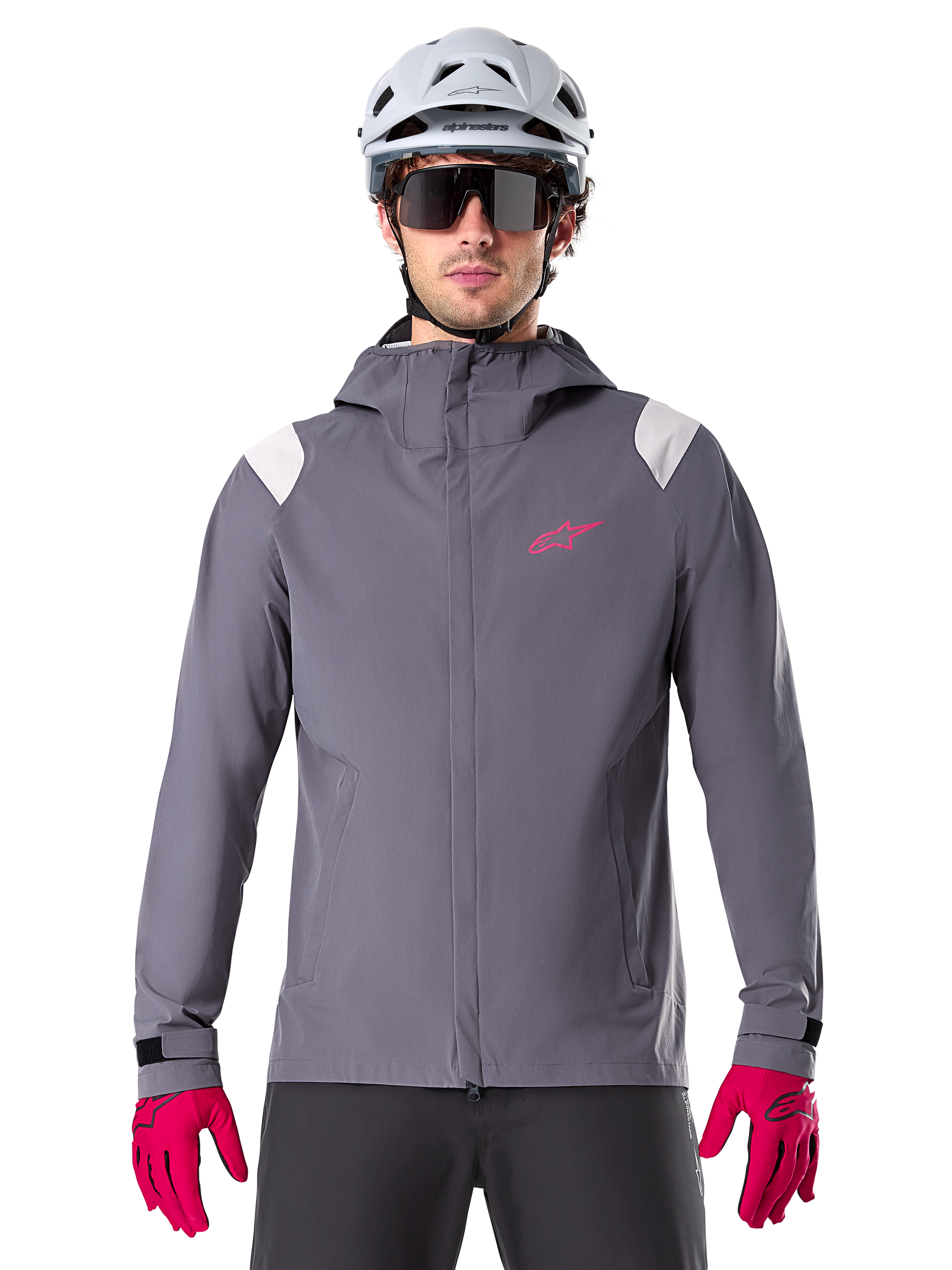 Alpinestars A-Dura regnjacka, MTB-regnjacka, mörk titangrå, design med huva, rosa Alpinestars-logotyp och ljusgrå axelpaneler, bärs med vit MTB-hjälm och starkt rosa handskar, vattentät utrustning för terrängcykling
