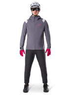 Alpinestars A-Dura regnjacka, mountainbikejacka, Dark Titanium-grå med rosa logotyp, bärs med grå MTB-hjälm och klarrosa handskar, skyddande 2,5-lagers membrankonstruktion för cykling i vått väder