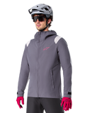 Alpinestars A-Dura regnjacka, regnjacka för mountainbike, mörkgrå med rosa logotyp och vita axeldetaljer, design med huva och framfickor, bärs med rosa handskar och en ljusgrå cykelhjälm