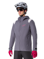 Alpinestars A-Dura regnjacka, regnjacka för mountainbike, mörkgrå med rosa logotyp och vita axeldetaljer, design med huva och framfickor, bärs med rosa handskar och en ljusgrå cykelhjälm