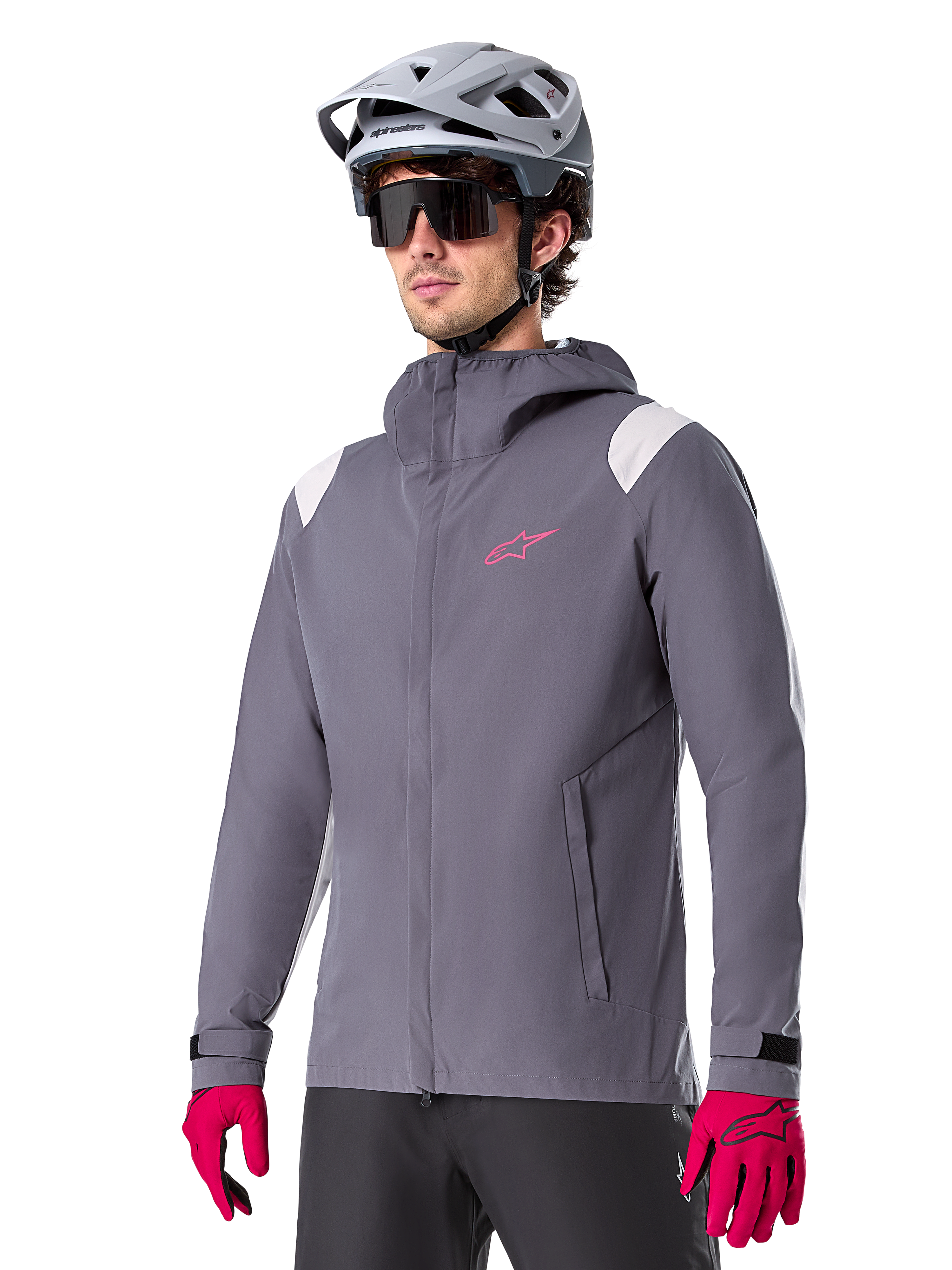 Alpinestars A-Dura regnjacka, regnjacka för mountainbike, mörkgrå med rosa logotyp och vita axeldetaljer, design med huva och framfickor, bärs med rosa handskar och en ljusgrå cykelhjälm