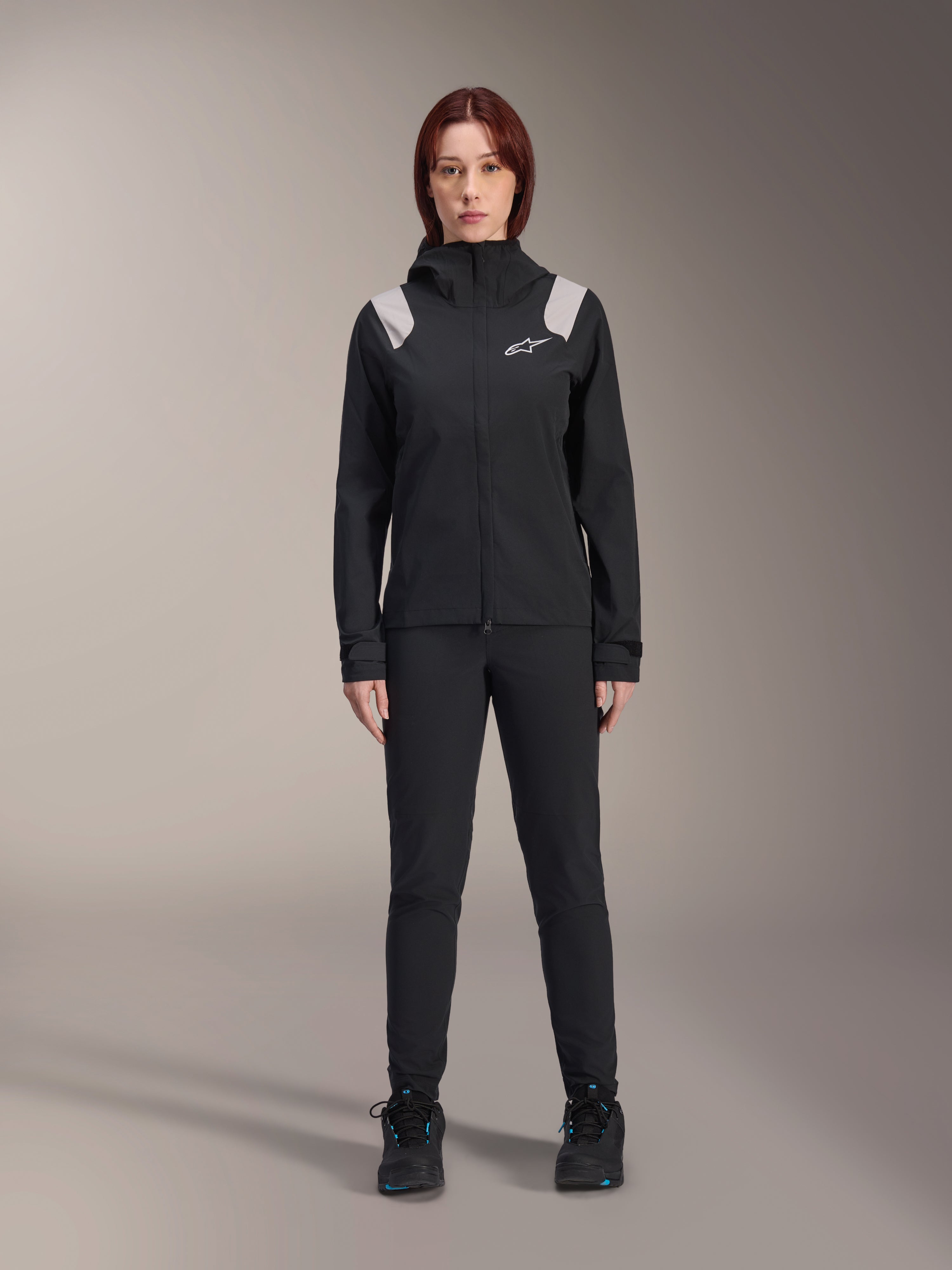Alpinestars Stella A-Dura regnjacka, MTB-regnjacka för damer, svart med ljusgrå axeldetaljer och vit logotyp, bärs med matchande svarta byxor och skor, försedd med huva och justerbara manschetter, designad för MTB-cykling