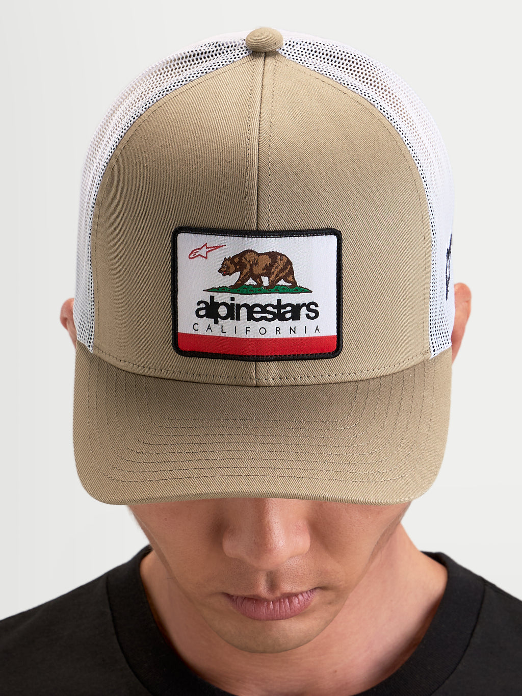 Alpinestars Cali 2.0 keps, trucker keps i khaki och vit, med strukturerad twillfront, Kalifornien-björnmärke, böjd skärm och ventilerande meshbakstycke på modell