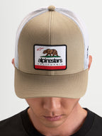Alpinestars Cali 2.0 keps, trucker keps i khaki och vit, med strukturerad twillfront, Kalifornien-björnmärke, böjd skärm och ventilerande meshbakstycke på modell