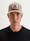Alpinestars Cali 2.0 keps, trucker-keps i khakifärg och vitt, med böjd skärm och Kalifornien-björnmärke på framsidan, bärs av en modell