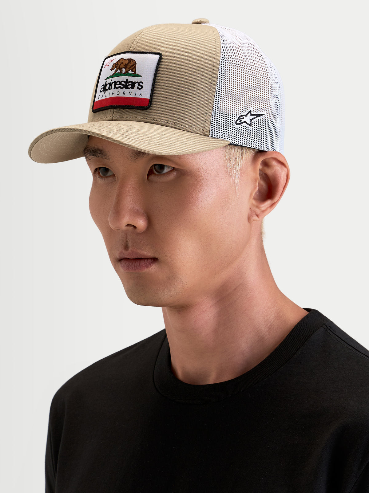 Alpinestars Cali 2.0 keps, khaki och vit trucker-keps med böjd skärm och vävt Kalifornien-märke, bärs av en modell