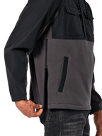 Alpinestars Juncture Hybrid-jacka i Black Gunmetal, sidodetalj som visar sidodragkedjan och den nedre kantfickan, design i mixade material med grå canvasfleece och svarta ripstop-överdrag, avslappnad motorsportinspirerad streetwear