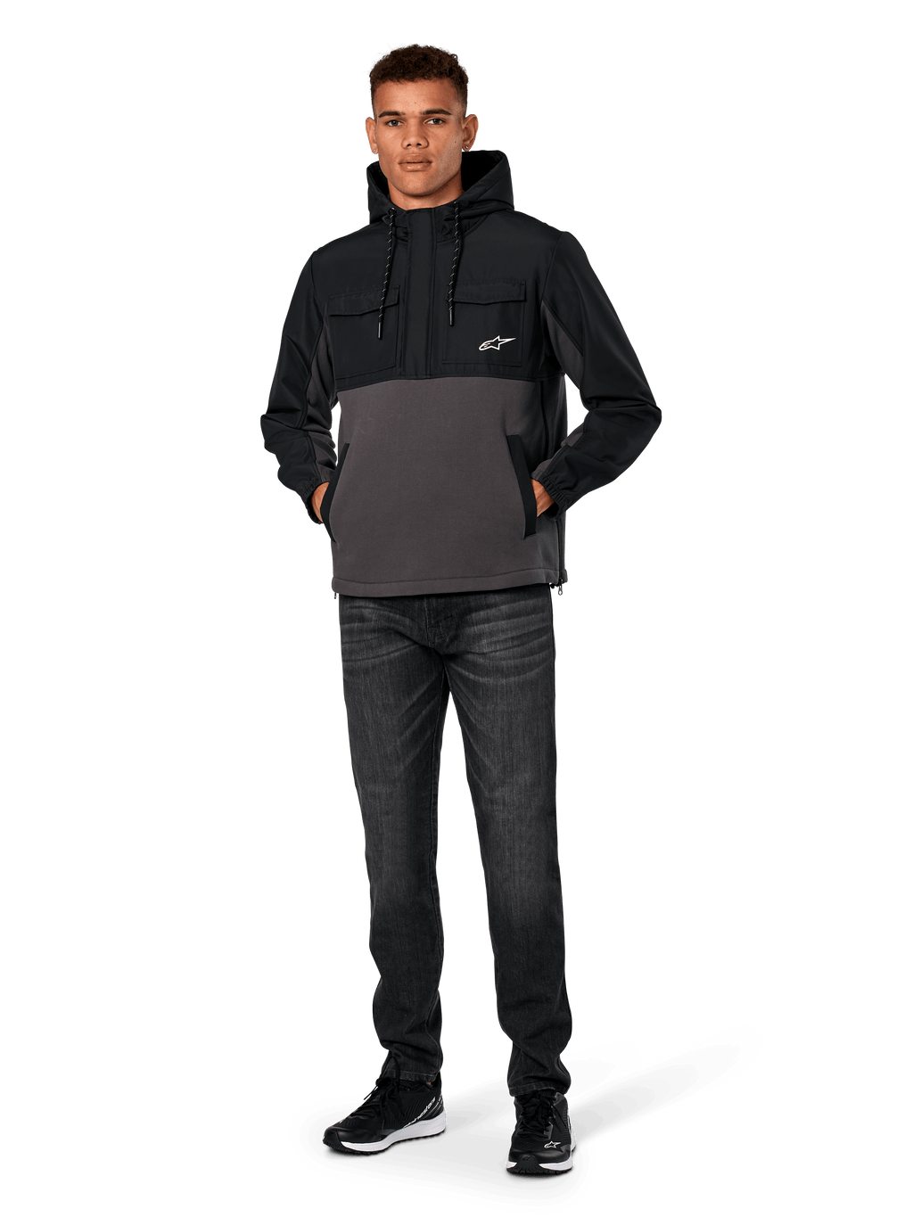 Alpinestars Juncture Hybrid-jacka, svart och gunmetal, anorak-hoodie i mixat material med kropp i canvasfleece och ripstop-överdrag, vit A-star-logotyp på bröstet, huva med dragsko, bärs av modell med mörka jeans och svarta sneakers, avslappnad motorsport-inspirerad streetwear