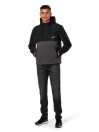 Alpinestars Juncture Hybrid-jacka, svart och gunmetal, anorak-hoodie i mixat material med kropp i canvasfleece och ripstop-överdrag, vit A-star-logotyp på bröstet, huva med dragsko, bärs av modell med mörka jeans och svarta sneakers, avslappnad motorsport-inspirerad streetwear