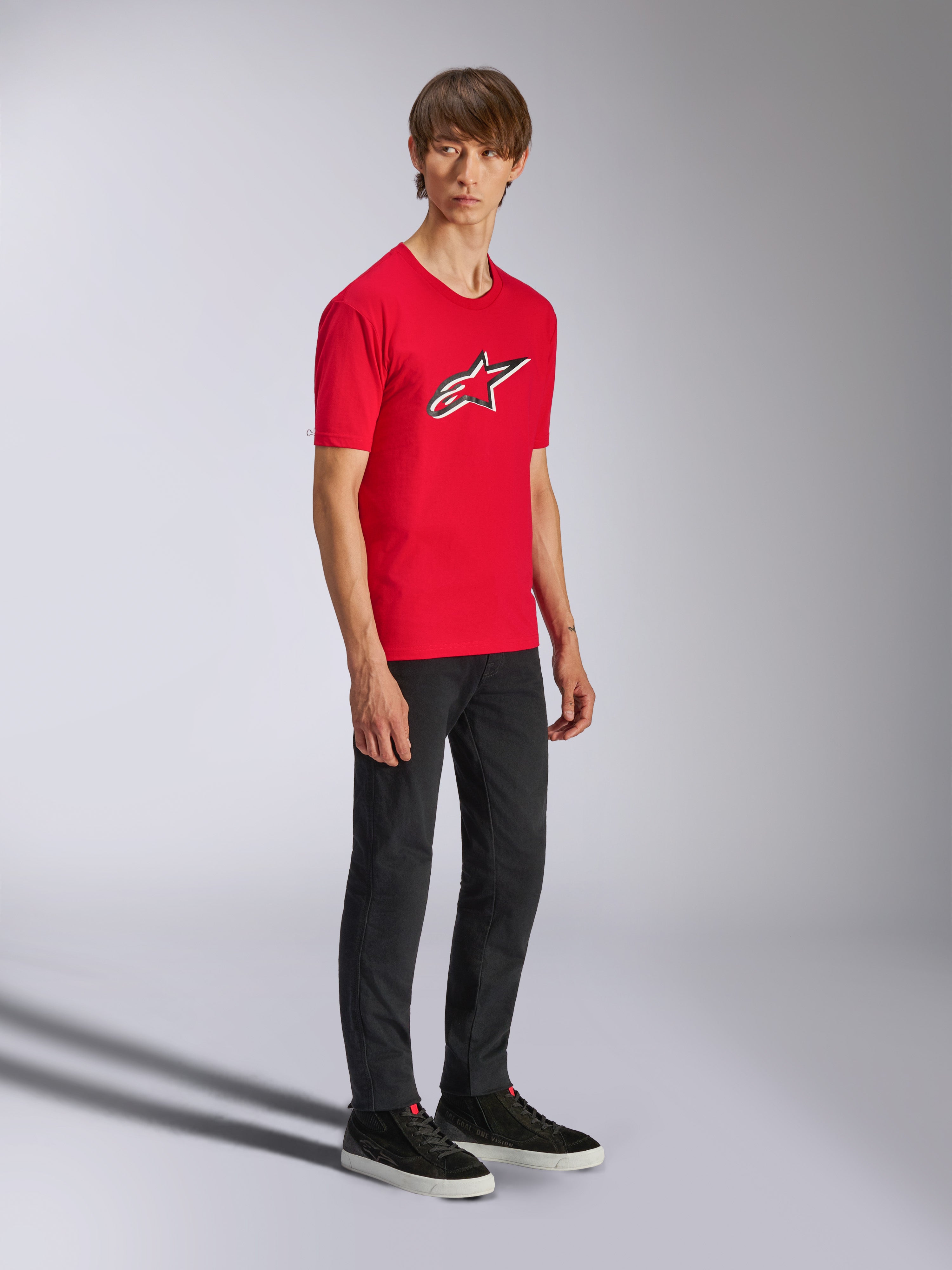 Alpinestars Ageless Shadow CSF Tee, röd kortärmad t-shirt, med en stor Ageless-logotyp på bröstet, bärs av en modell med svarta byxor och sneakers, avslappnad motorsport-streetwear
