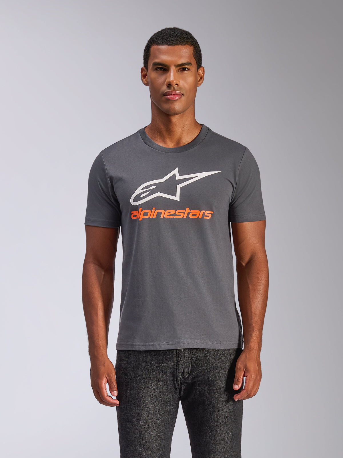 Alpinestars Always 2.0 CSF Tee, mörkgrå kortärmad t-shirt, stor vit A-stjärna logotyp med orange Alpinestars-text, bärs av en man, casual motorsport streetwear