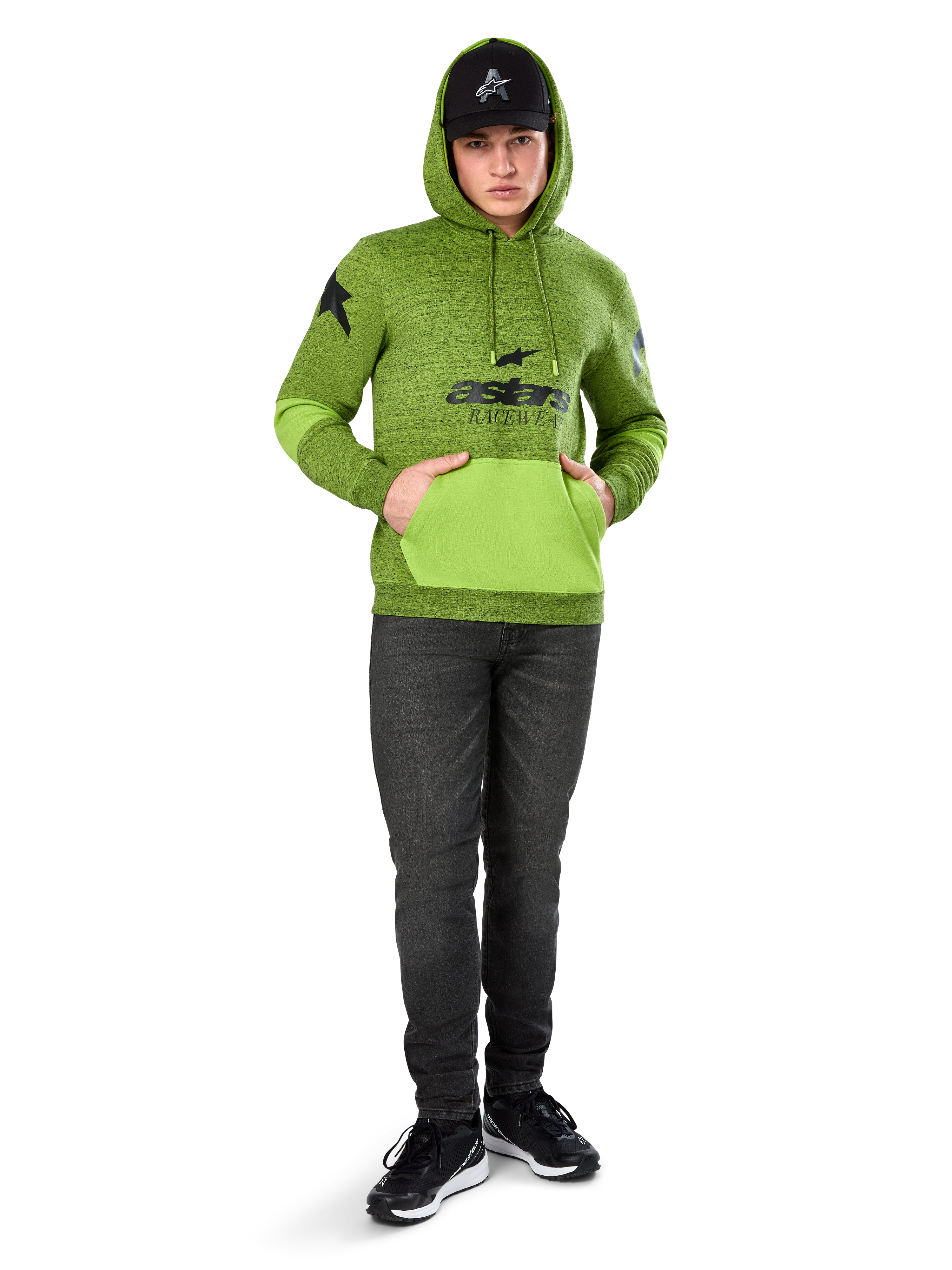 Alpinestars Perpetuate Hoodie, limegrön melerad fleece i pullovermodell med kontrasterande klargrön känguruficka och ärmpaneler, svart 'astars'-grafik framtill, stylad med svart keps och mörka jeans, avslappnad motorsport-inspirerad streetwear