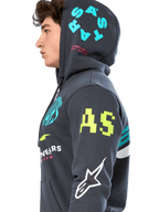 Alpinestars Variegate Hoodie, mörkgrå (Gunmetal) fleecehoodie med dragkedja, sidoprofil av modell, grafik med flera logotyper i neongult, ljusblått och vitt, 'AS'-logotyp på ärmen och 'STARS' på huvan, vardaglig motorsportinspirerad streetwear