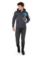 Alpinestars Variegate Hoodie, fleecehoodie med dragkedja framtill, gunmetal-grå, bärs av modell med svarta jeans och sneakers, med turkos 'ASTARS'-märkning och färgglad logografik på ärmar och bröst, avslappnad motorsportinspirerad streetwear