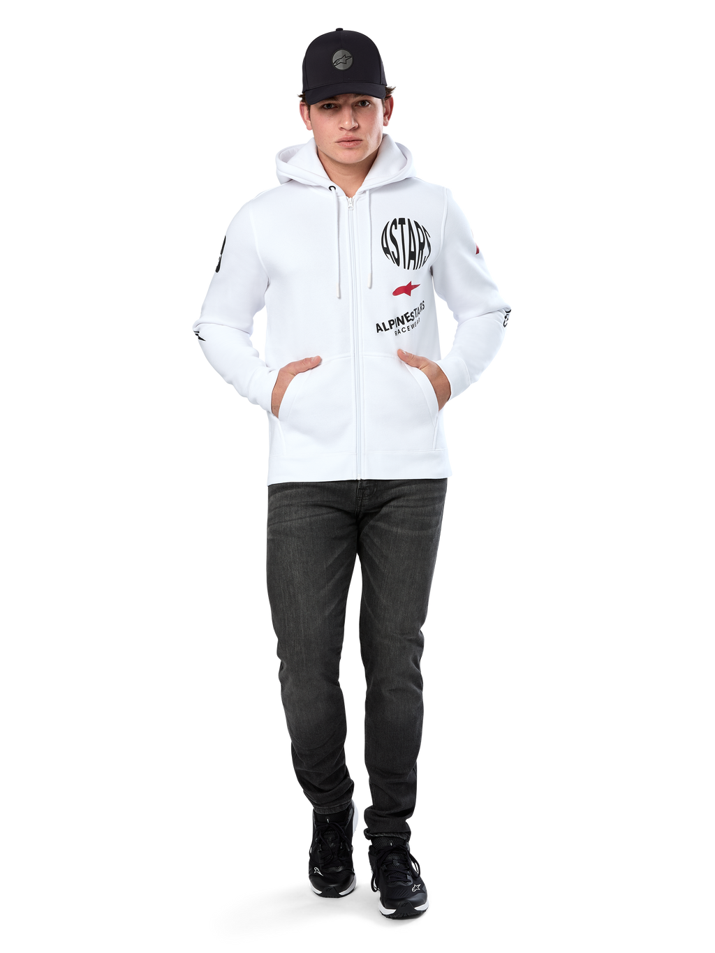 Alpinestars Variegate Hoodie, vit fleecehoodie med dragkedja, grafik med flera logotyper inklusive 'ASTARS' och röd stjärnlogotyp på bröstet, grafiska detaljer på ärmarna, bärs av modell med svart keps och svarta jeans, avslappnat motorsport-streetwear