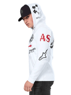 Alpinestars Variegate Hoodie, vit fleecehoodie med dragkedja framtill, grafik med flera logotyper på ärmarna och huvan med röda 'AS'-bokstäver och en svart stjärnlogotyp, bärs av en man med en svart keps, avslappnad motorsport-streetwear