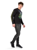 Man som bär Alpinestars Ayess CSF långärmad t-shirt, svart, med gul text på ärmarna och livfull grafik i lime och cyan på bröstet, kombinerat med mörkgrå jeans och svarta sneakers, avslappnad motorsportinspirerad streetwear.