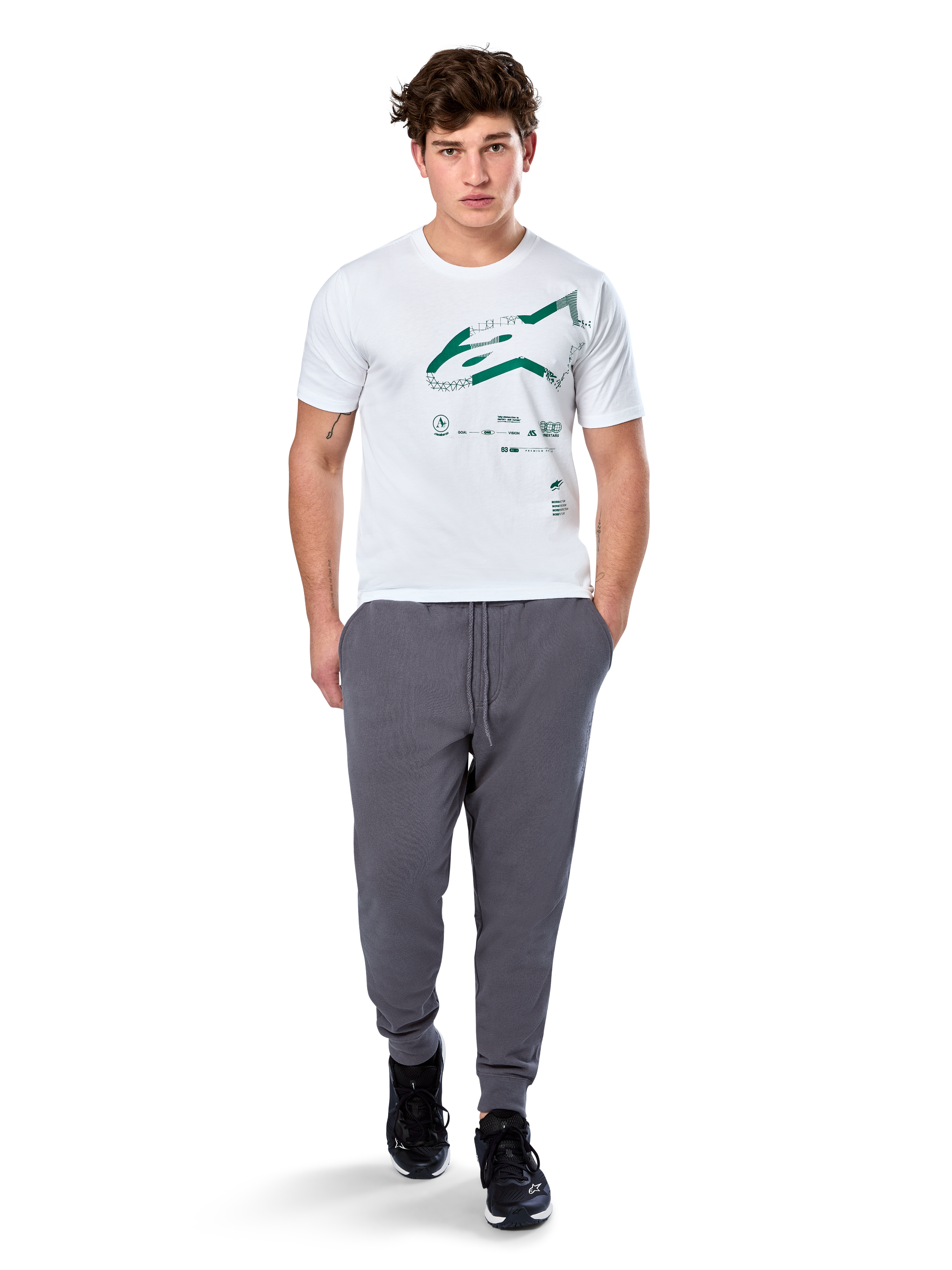 Alpinestars Geografica CSF Tee, kortärmad T-shirt, vit, grön Astars-logotyp med geografisk multi-tech-grafik, bärs med grå mjukisbyxor och svarta sneakers, avslappnad motorsport-streetwear