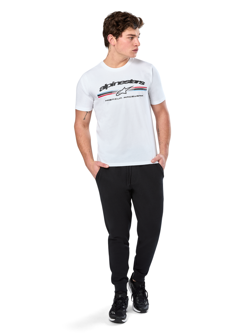 Alpinestars Prevail CSF Tee, kortärmad t-shirt, vit, med en paddockinspirerad logotyp med trefärgade ränder och Alpinestars-branding framtill, bärs av en modell med svarta joggers och svarta sneakers, avslappnad motorsport-streetwear