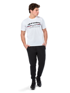 Alpinestars Prevail CSF Tee, kortärmad t-shirt, vit, med en paddockinspirerad logotyp med trefärgade ränder och Alpinestars-branding framtill, bärs av en modell med svarta joggers och svarta sneakers, avslappnad motorsport-streetwear