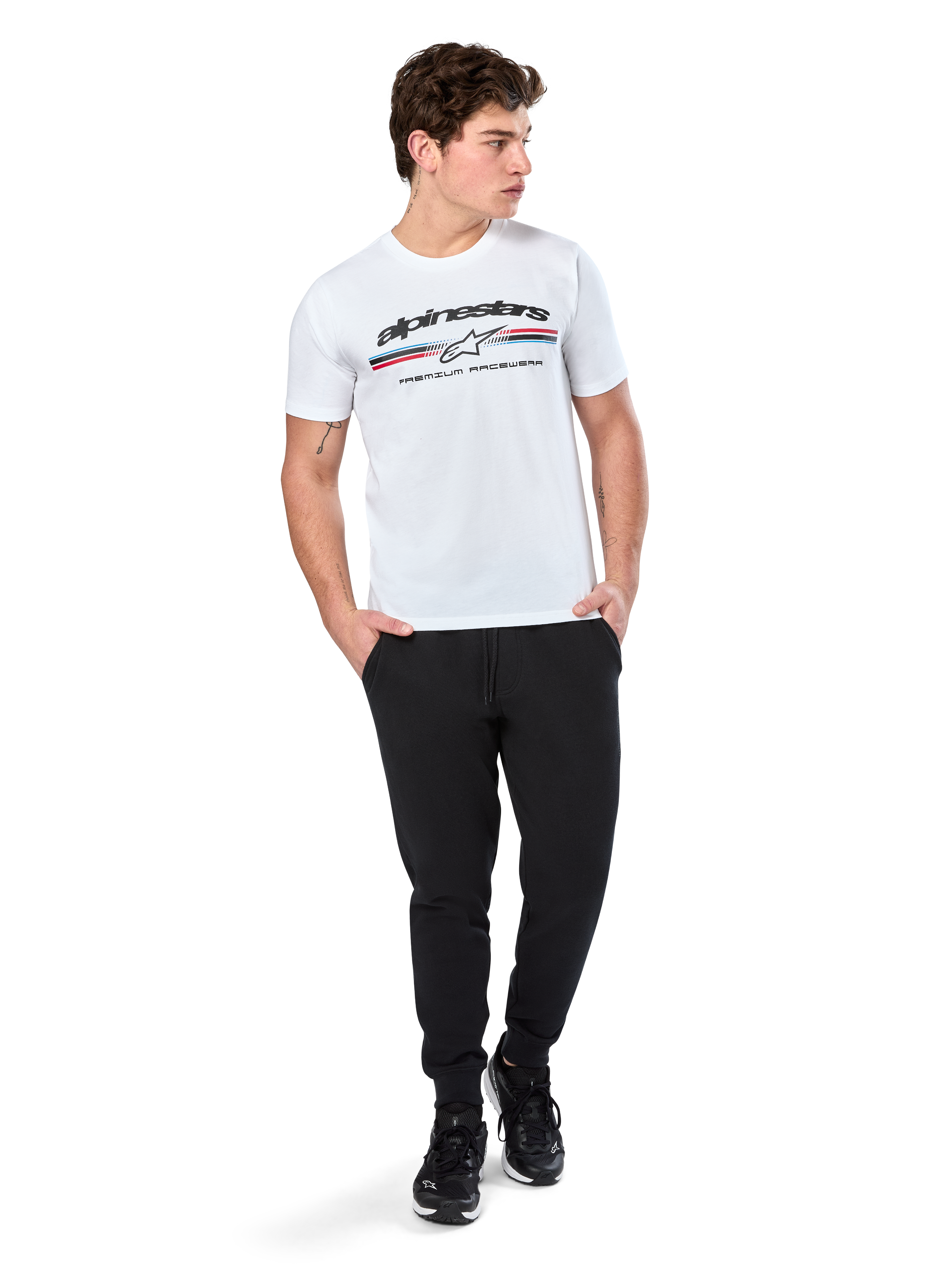 Alpinestars Prevail CSF Tee, kortärmad t-shirt, vit, med en paddockinspirerad logotyp med trefärgade ränder och Alpinestars-branding framtill, bärs av en modell med svarta joggers och svarta sneakers, avslappnad motorsport-streetwear